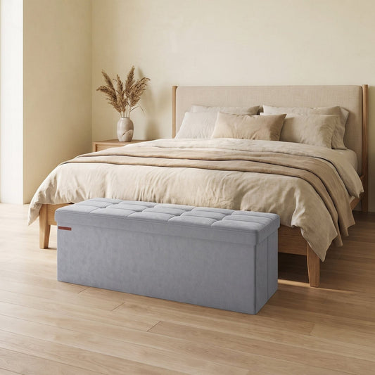 Banc coffre en velours gris clair au pied d'un lit dans une chambre claire