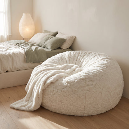 Pouf géant XXL blanc dans une chambre, plaid posé au pied du lit